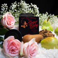 Load image into Gallery viewer, A candle product labeled 'Two Hot THOTS Candle Co. Sugar Baby' is styled in a flat lay with pink roses, pears, brown sugar, and white flowers on a dark background.